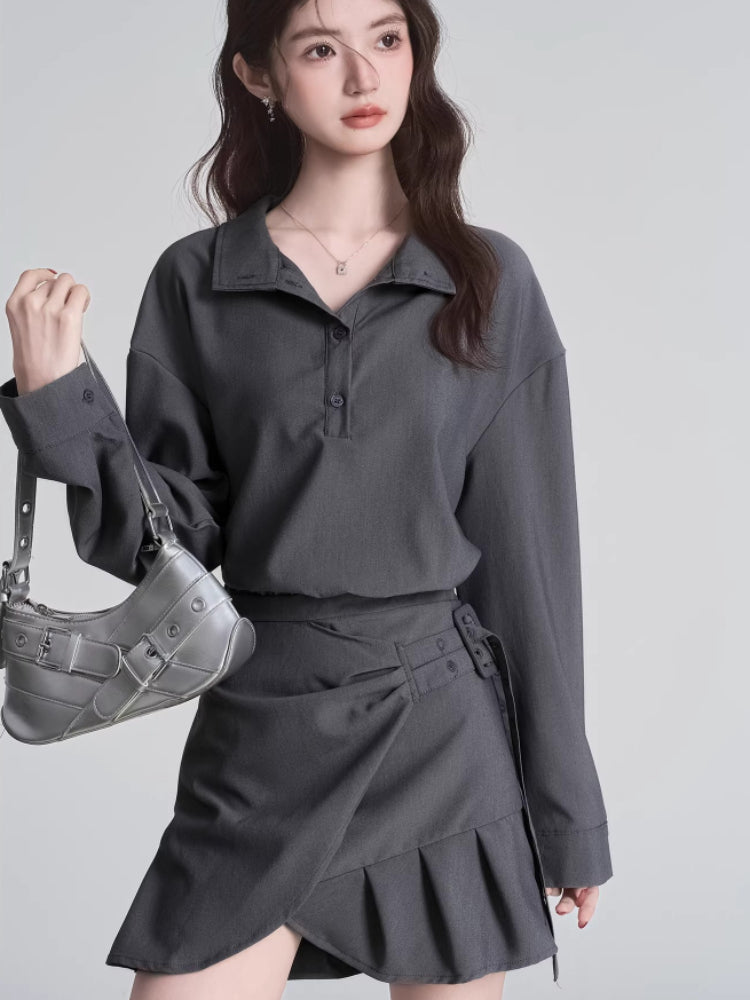 Model holding a silver handbag and wearing a grey long-sleeved collared shirt and a grey skirt.