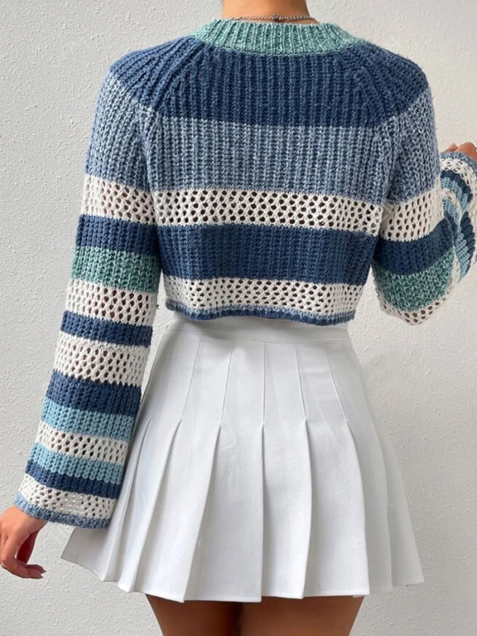 Back view of a woman wearing a blue and white striped crochet knit cropped sweater with bell sleeves, paired with a white pleated mini skirt. Secondary image