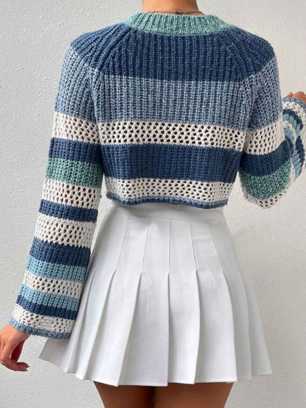 Back view of a woman wearing a blue and white striped crochet knit cropped sweater with bell sleeves, paired with a white pleated mini skirt.