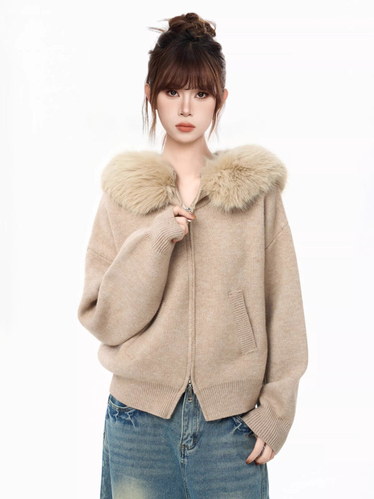 Woman wearing a beige knit cardigan with a faux fur collar and blue jeans, adjusting zipper