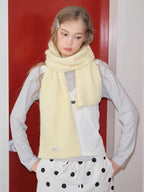 Model wearing a light yellow ribbed knit scarf draped around their neck, paired with a light grey long-sleeved shirt and white polka dot pants.