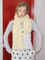 Model wearing a light yellow ribbed knit scarf draped around their neck, paired with a light grey long-sleeved shirt and white polka dot pants.