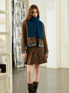 Model wearing a brown tweed jacket, denim shirt, blue scarf, and brown pleated skirt.