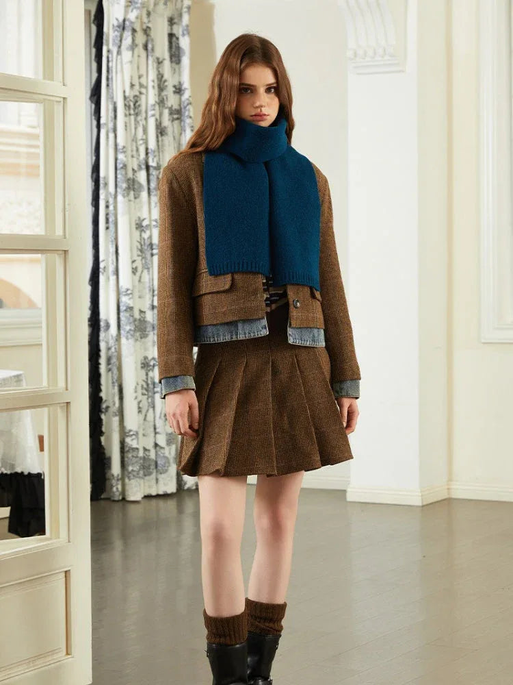 Model wearing a brown tweed jacket, denim shirt, blue scarf, and brown pleated skirt.
