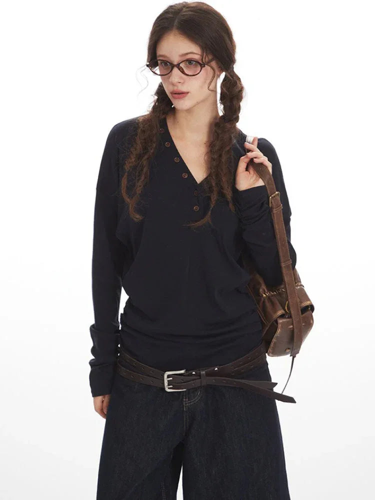 Close-up of a woman wearing a dark long-sleeved V-neck top and holding a brown leather crossbody bag, posing against a white background.