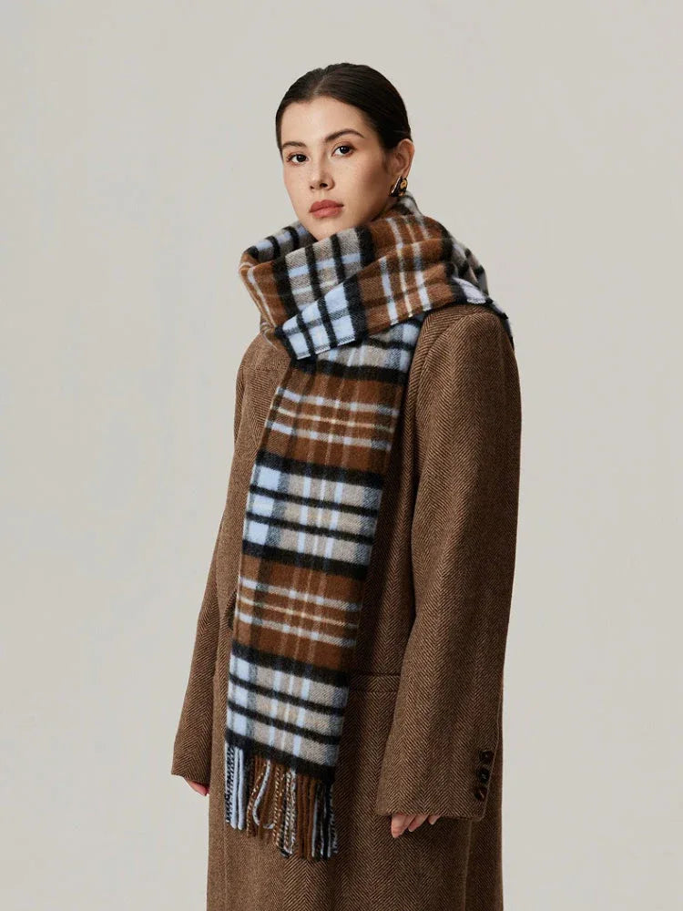 Woman in a brown coat with a brown plaid scarf featuring blue and black details, shown from the side.