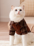 A white cat wearing a brown plaid shirt with a collar.