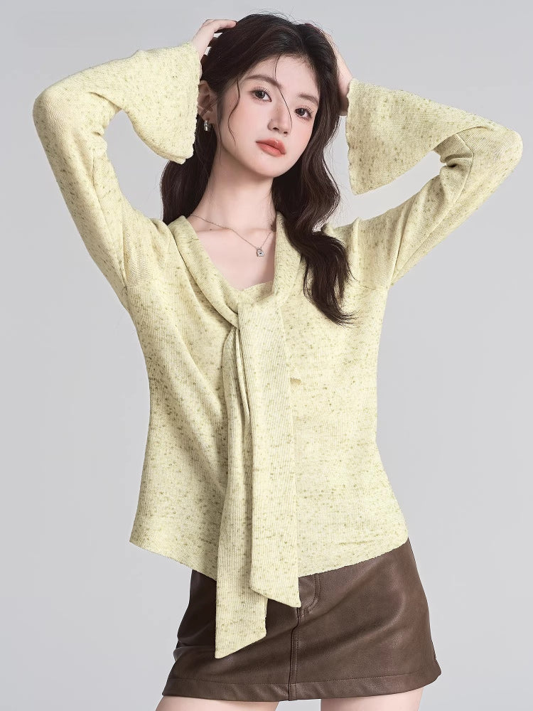 Woman posing with hands behind her head, wearing a light yellow textured knit top with a draped neckline and bell sleeves.