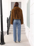 Back view of a woman wearing a brown faux fur cropped jacket and blue jeans, standing on stairs.