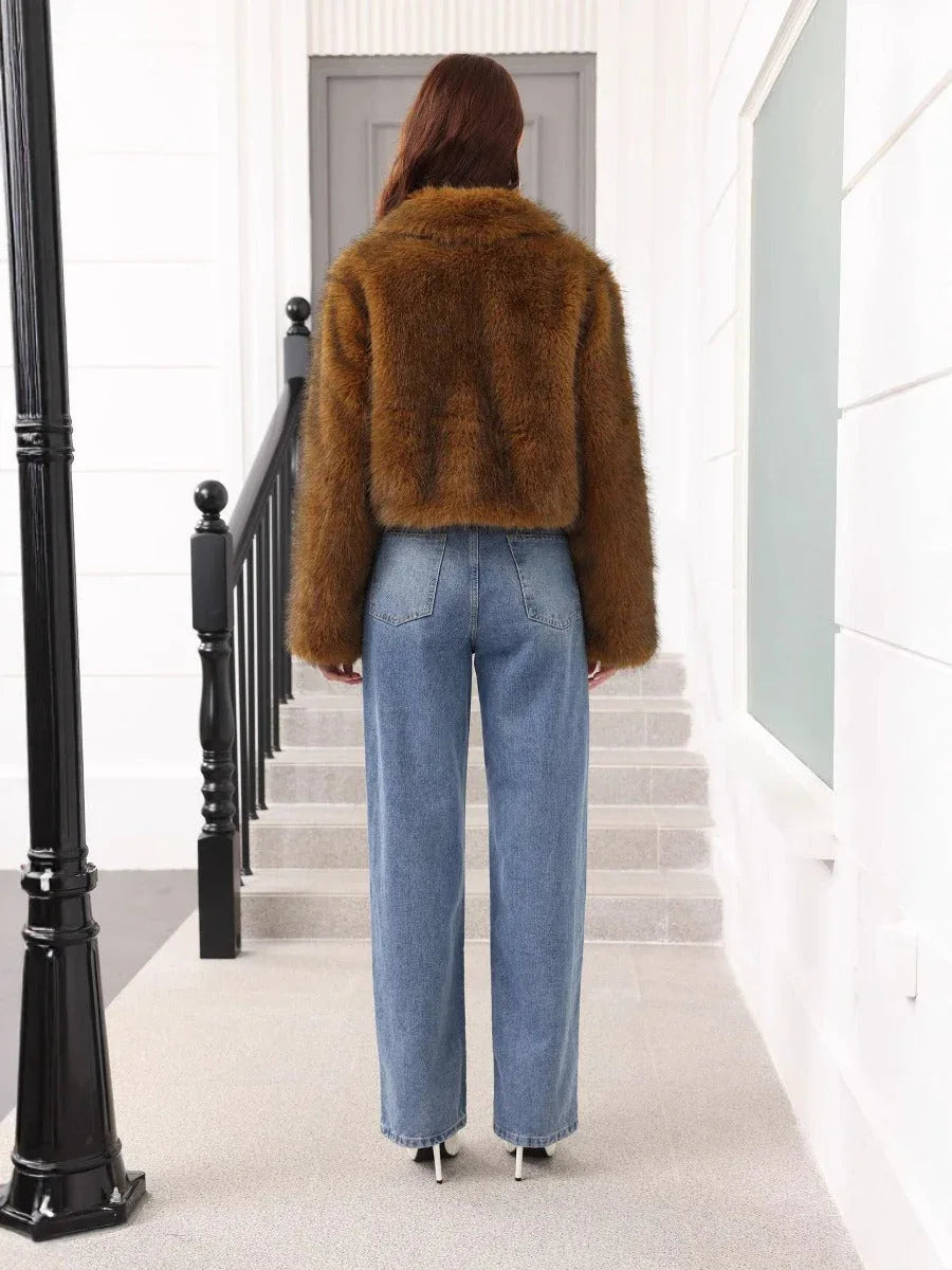 Back view of a woman wearing a brown faux fur cropped jacket and blue jeans, standing on stairs.