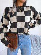 Woman wearing a black and white checkerboard knit sweater with light wash jeans and a brown fringe clutch, front view, showing more of the sweater.