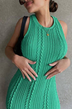 Close-up of a woman wearing a green sleeveless cable knit midi dress, hands on her stomach.