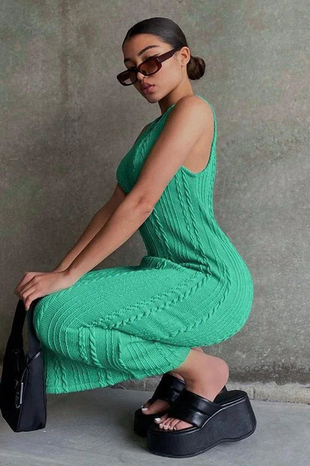 Woman in a green sleeveless cable knit midi dress, black platform sandals, and sunglasses, in a crouching pose.