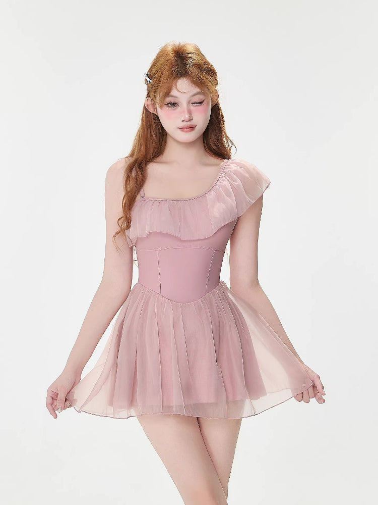 Front view of a woman modeling a pink one-shoulder swimsuit with a sheer skirt overlay.