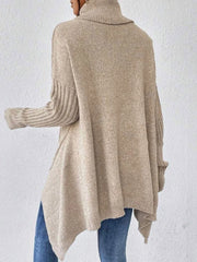 Back view of a woman wearing a beige oversized turtleneck sweater with an asymmetrical hem and ribbed sleeves.