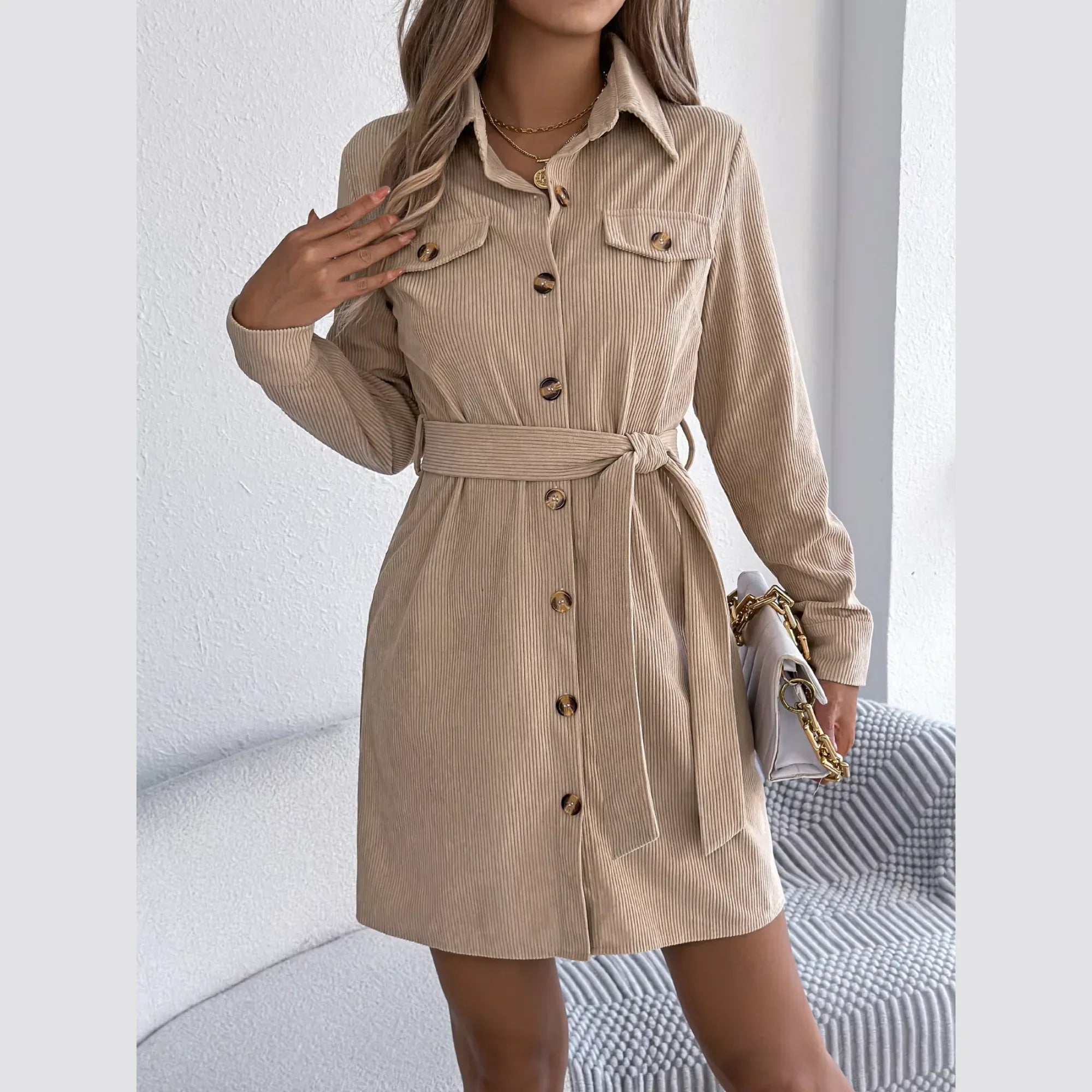 Woman wearing a tan corduroy shirt dress with a belted waist and collared neckline.