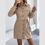 Woman holding a white quilted handbag and a phone while wearing a tan corduroy shirt dress.