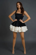 Full body shot of a model in a black and white dress with a ruffled hem, hands on hips.