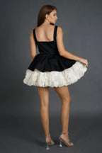 Back view of a model in a black and white dress with a square neckline and a ruffled hem.