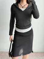 Full body shot of a woman in a casual outfit featuring a dark grey hooded zip-up top, white tank, and black skirt.