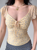 Detail of the neckline and bust of a yellow floral print mesh top with a ruched tie front.