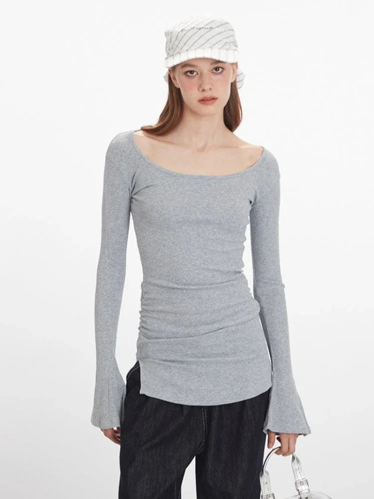 Front view of a woman wearing a grey long-sleeve ribbed knit top with bell sleeves and dark wash wide-leg jeans, accessorized with a striped headscarf.