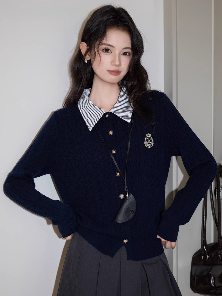 Woman posing in a navy blue cable knit cardigan with a striped collar and a gray pleated skirt.