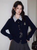 Woman posing in a navy blue cable knit cardigan with a striped collar and a gray pleated skirt.