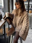 woman wearing a beige chunky cable knit oversized sweater with black tights and brown boots, holding a coffee cup