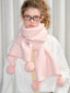Woman wearing a pink fuzzy knit scarf with pom-pom embellishments and glasses.