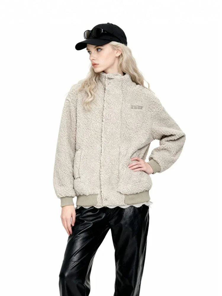 Woman in a cream-colored sherpa fleece bomber jacket, black faux leather pants, and a black baseball cap with sunglasses, posing with hand on hip.