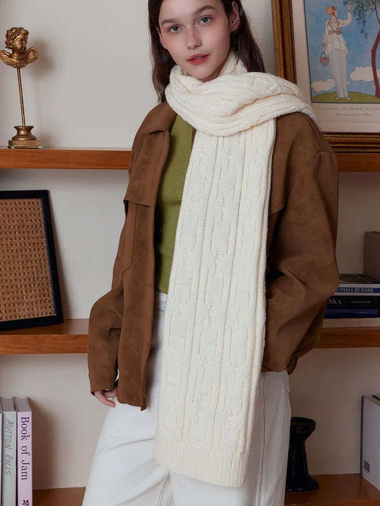 Woman posing with a cream-colored cable knit scarf in front of shelves.