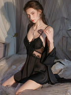 Woman wearing a black satin babydoll nightgown with lace detailing and a matching robe, posing on a bed.
