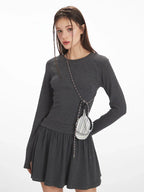 Close-up of a woman wearing a dark grey long-sleeve mini dress with a gathered waist and a small striped pouch around her neck.