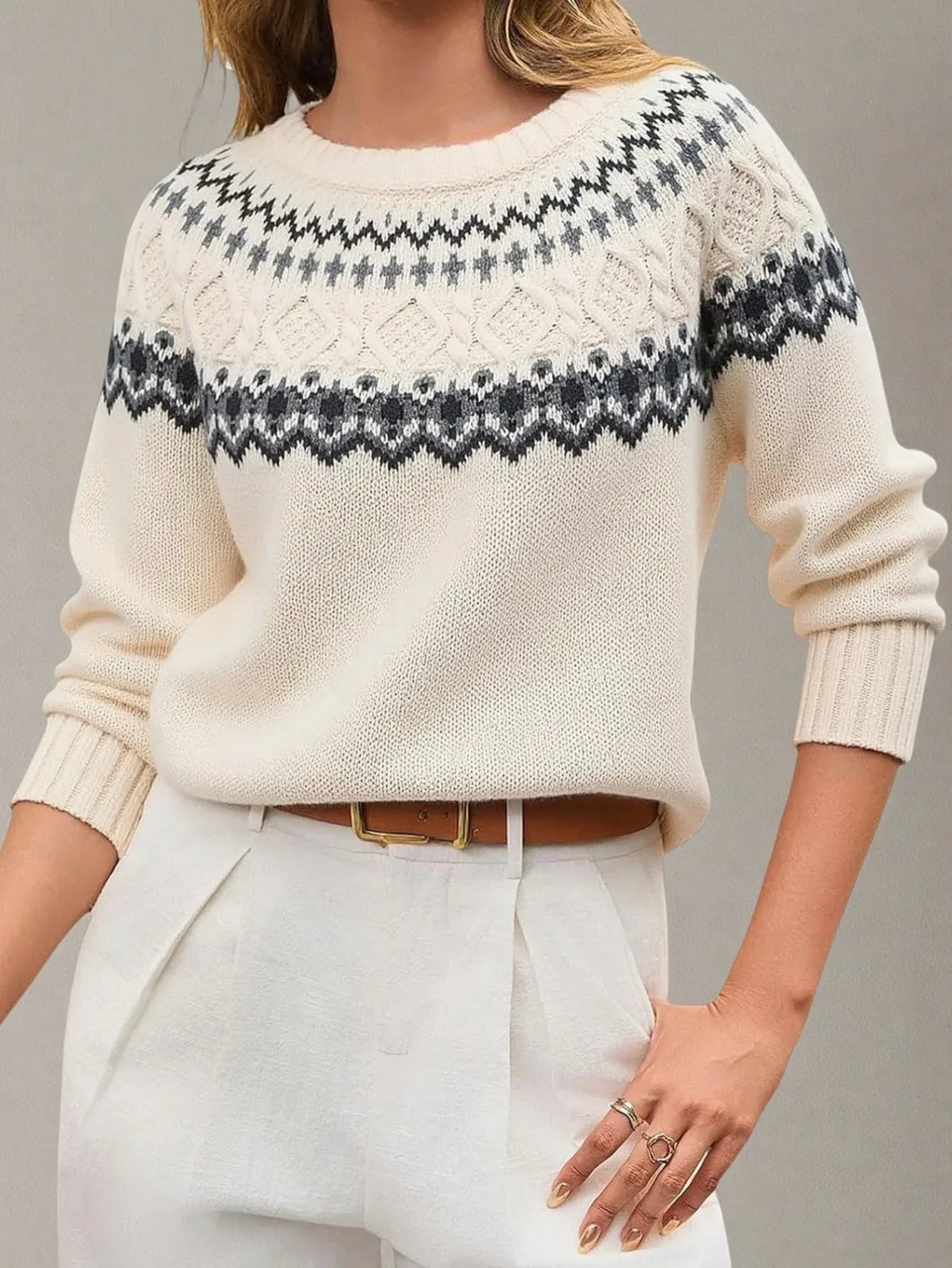 Woman wearing a cream-colored knit sweater with a Fair Isle pattern around the yoke and white trousers with a brown belt.