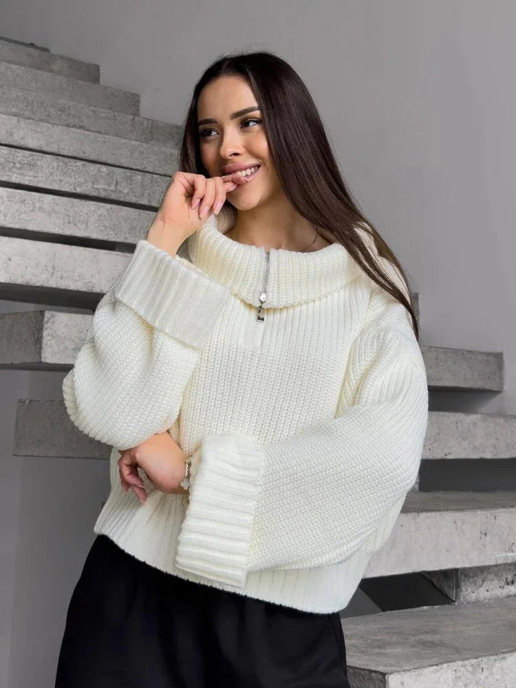 Woman wearing a cream-colored oversized knit sweater with a half-zip neckline and wide sleeves, smiling.