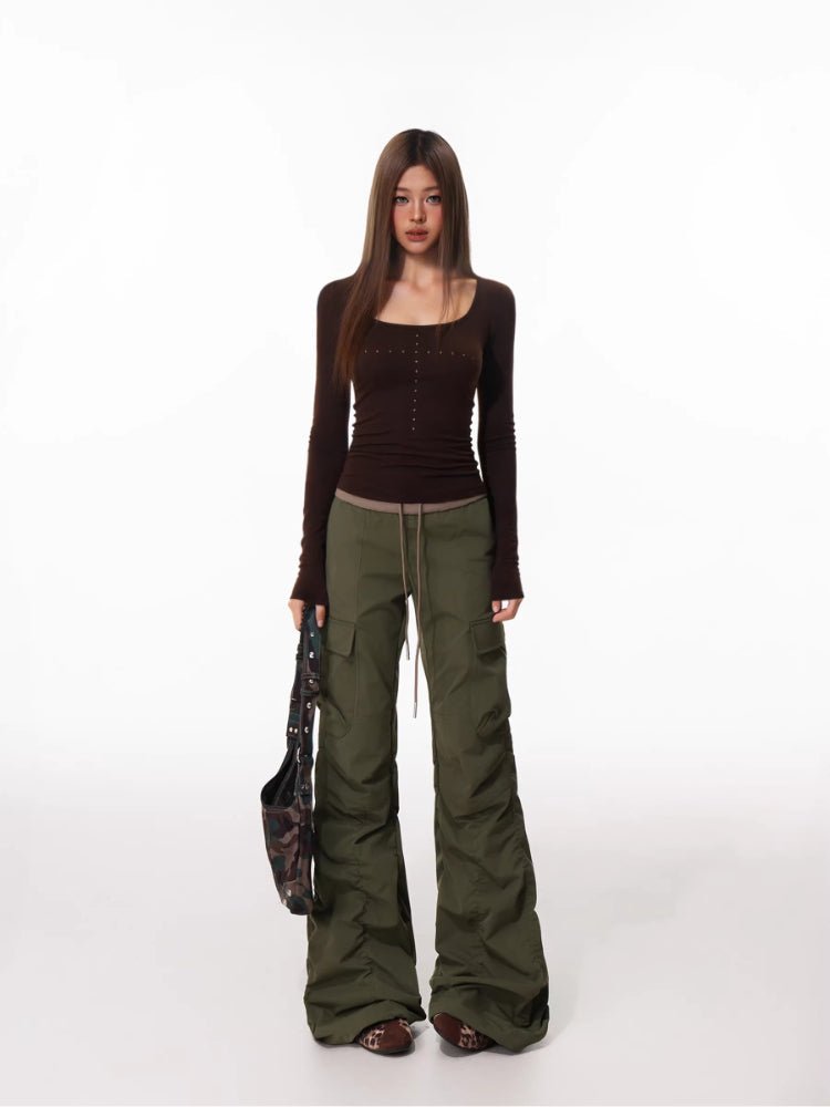 Full body shot of a woman in a brown long-sleeved top and olive green cargo pants holding a patterned bag.
