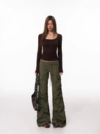 Full body shot of a woman in a brown long-sleeved top and olive green cargo pants holding a patterned bag.