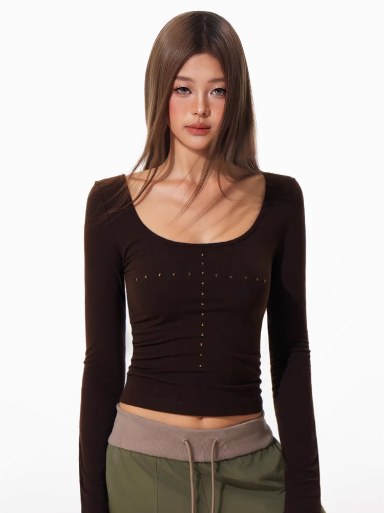 Close-up of a woman's chest wearing a brown long-sleeved top with decorative studs.