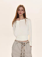 Woman wearing an off-white crew neck knit sweater with a ribbed hem, paired with beige cargo pants and a patterned belt.