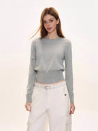 Woman wearing a light grey crew neck knit sweater with a ribbed hem, paired with white cargo pants and a white belt.