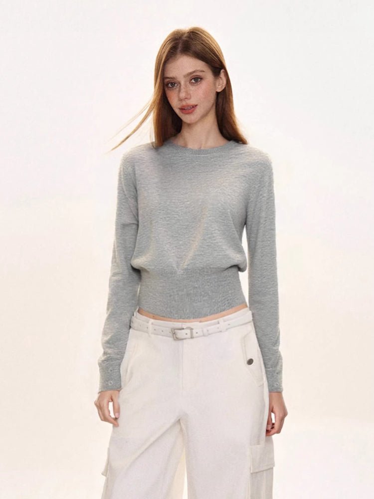 Woman wearing a light grey crew neck knit sweater with a ribbed hem, paired with white cargo pants and a white belt.