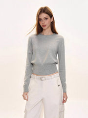 Woman wearing a light grey crew neck knit sweater with a ribbed hem, paired with white cargo pants and a white belt.