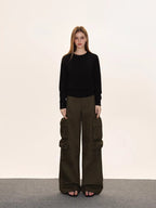Full body shot of a woman in a black crew neck knit sweater with a ribbed hem, olive green cargo pants, and black sandals.