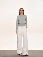 Full body shot of a woman in a light grey crew neck knit sweater with a ribbed hem, white cargo pants, and black sandals.