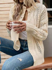 Woman wearing a cream cable knit cardigan with blue distressed jeans and holding a white paper cup.