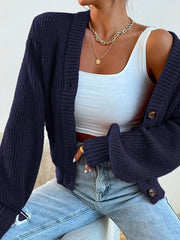 Front view of a woman wearing a navy blue oversized knit cardigan over a white tank top and ripped blue jeans, with gold necklaces.
