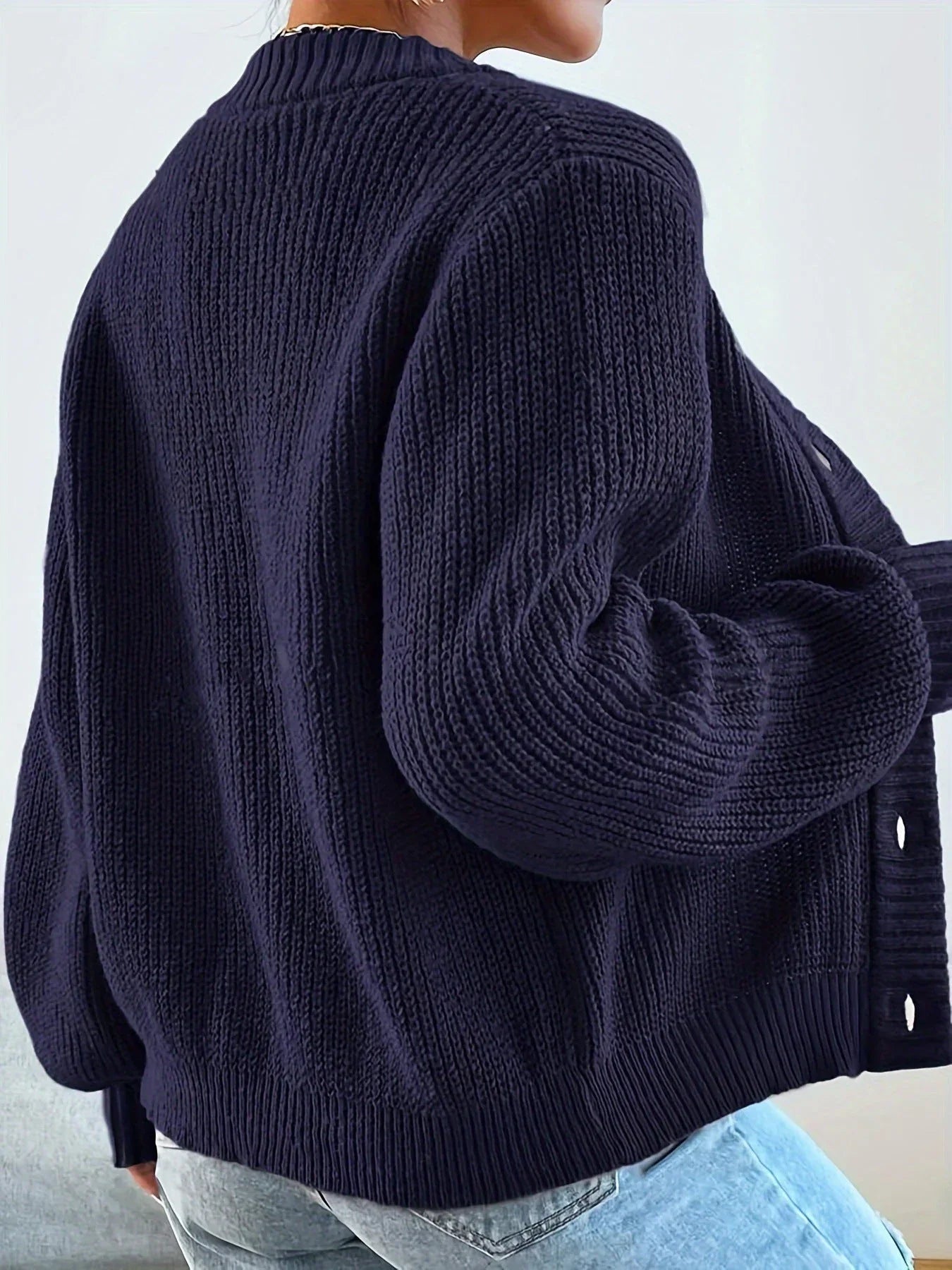 Back view of a woman wearing a navy blue oversized knit cardigan, showing the ribbed texture and balloon sleeves.