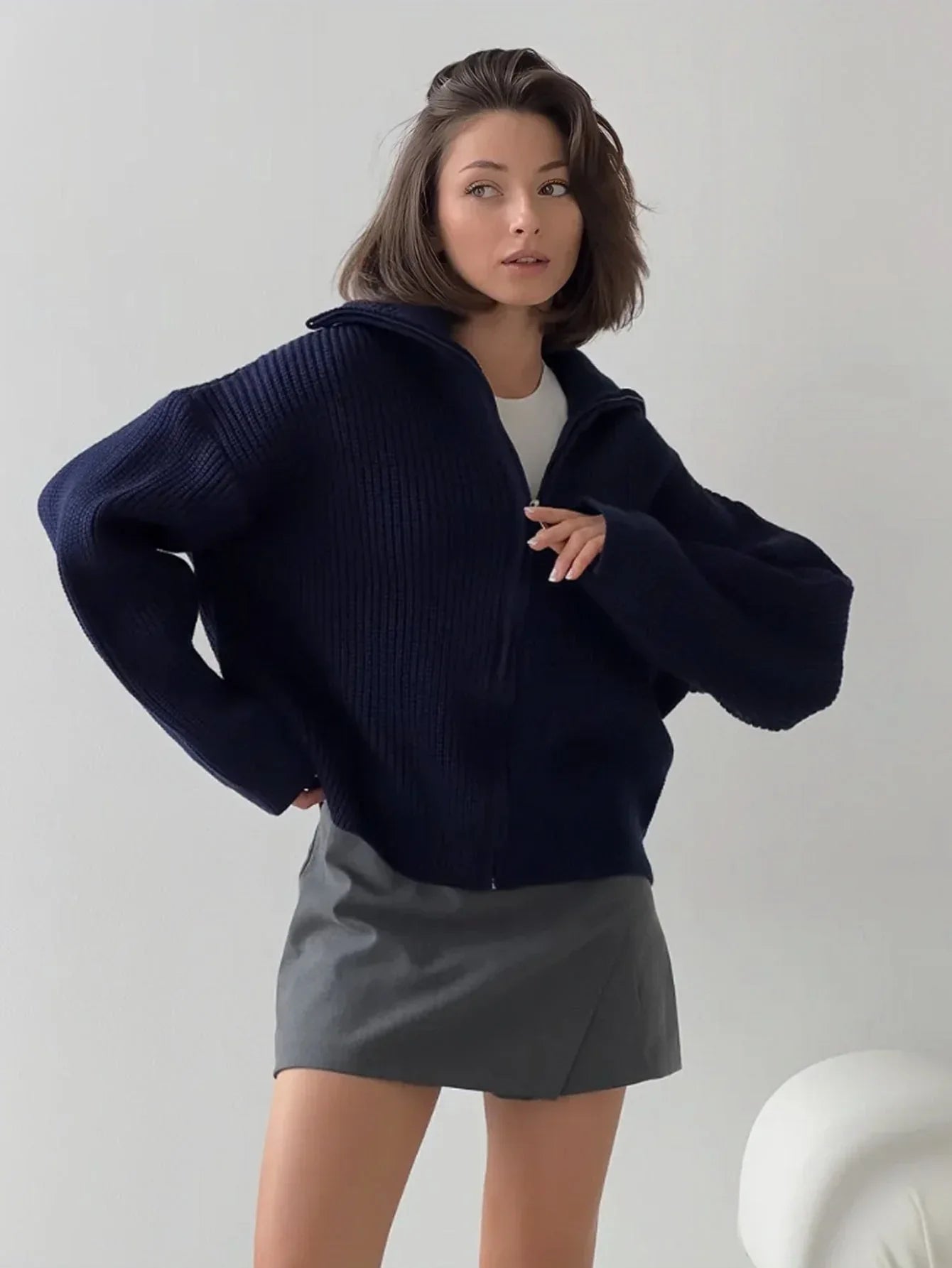 Woman wearing a navy blue zip-up cardigan over a white top and gray mini skirt.