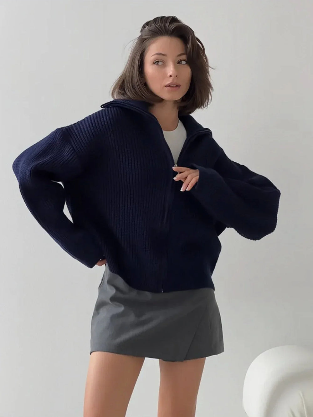 Woman wearing a navy blue zip-up cardigan over a white top and gray mini skirt.